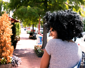 A smiling woman with black, coily African American hair, walking down a street.