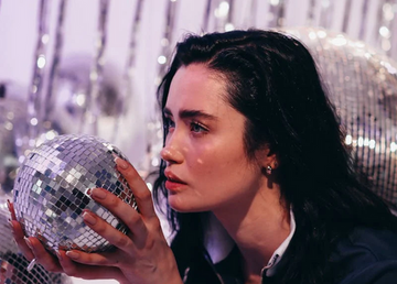 A young woman with black, slicked-back hair holding a disco ball.