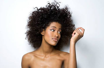 A darker-skinned female holds out and stares at a piece of her medium hair. Source: iStock