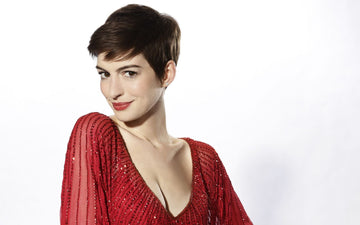 Woman with dark hair in a pixie cut, wearing a red top, smiling at the camera against a white backdrop.