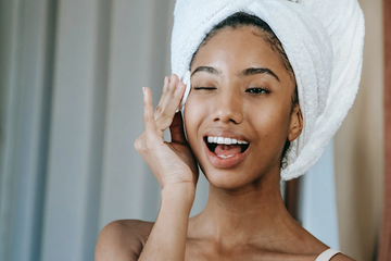 image of a girl with a towel on her hair, doing self care in the mirror.