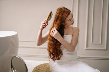 Woman with red, wavy hair sitting brushing hair