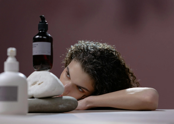 Image of a girl with brown curly hair looking at a shampoo bottle. Taken from Pexels.
