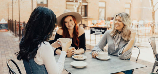 3 women sitting at table having coffee and laughing with TYME curls