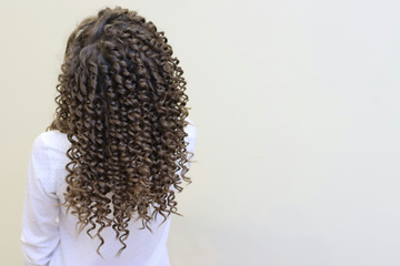 Woman with long curly hair walking down a city street.
