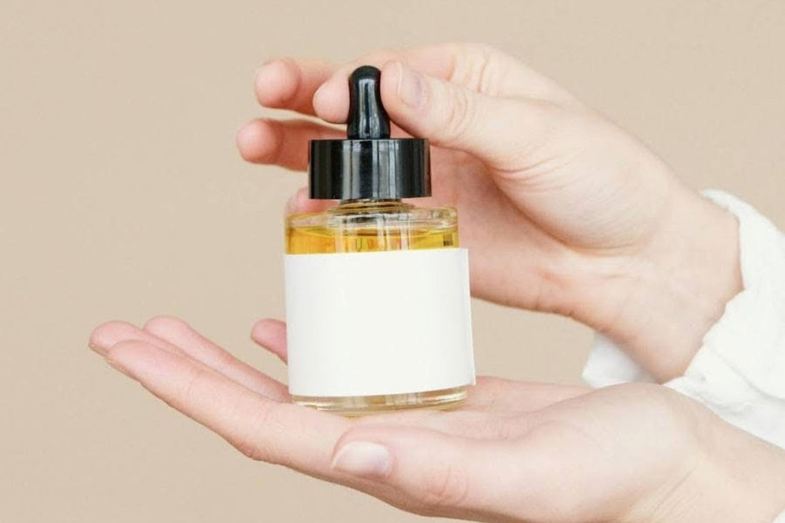 A woman’s hands holding a yellow-colored hair oil in a clear bottle with a black lid. SourceL Pexels.