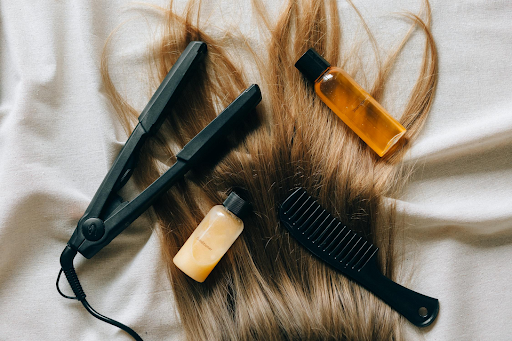 (Image of a flat iron on hair with hair products. Taken from Pexels)
