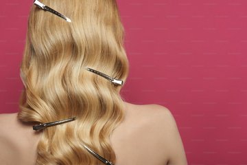 The back of a woman’s head, featuring shiny and wavy long blonde hair with clips in.