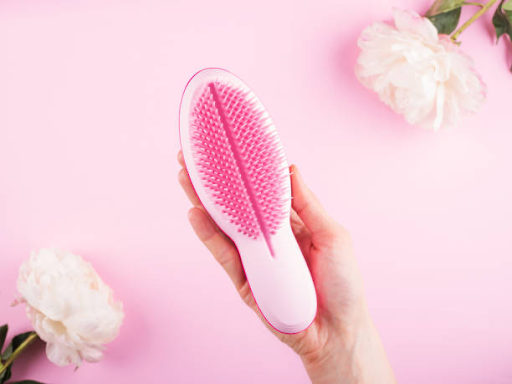 Image of a person holding a detangling hairbrush against a pink backdrop.