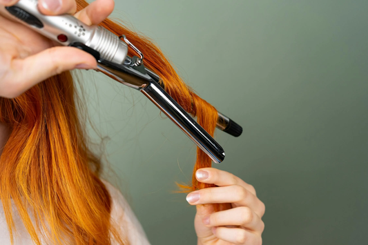 A close-up of a redhead woman using an affordable curling iron on her hair.