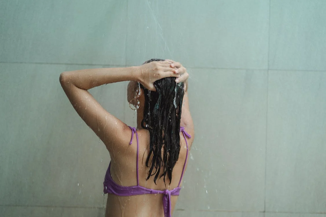 A woman showering in her bathing suit, rinsing shampoo out of her hair