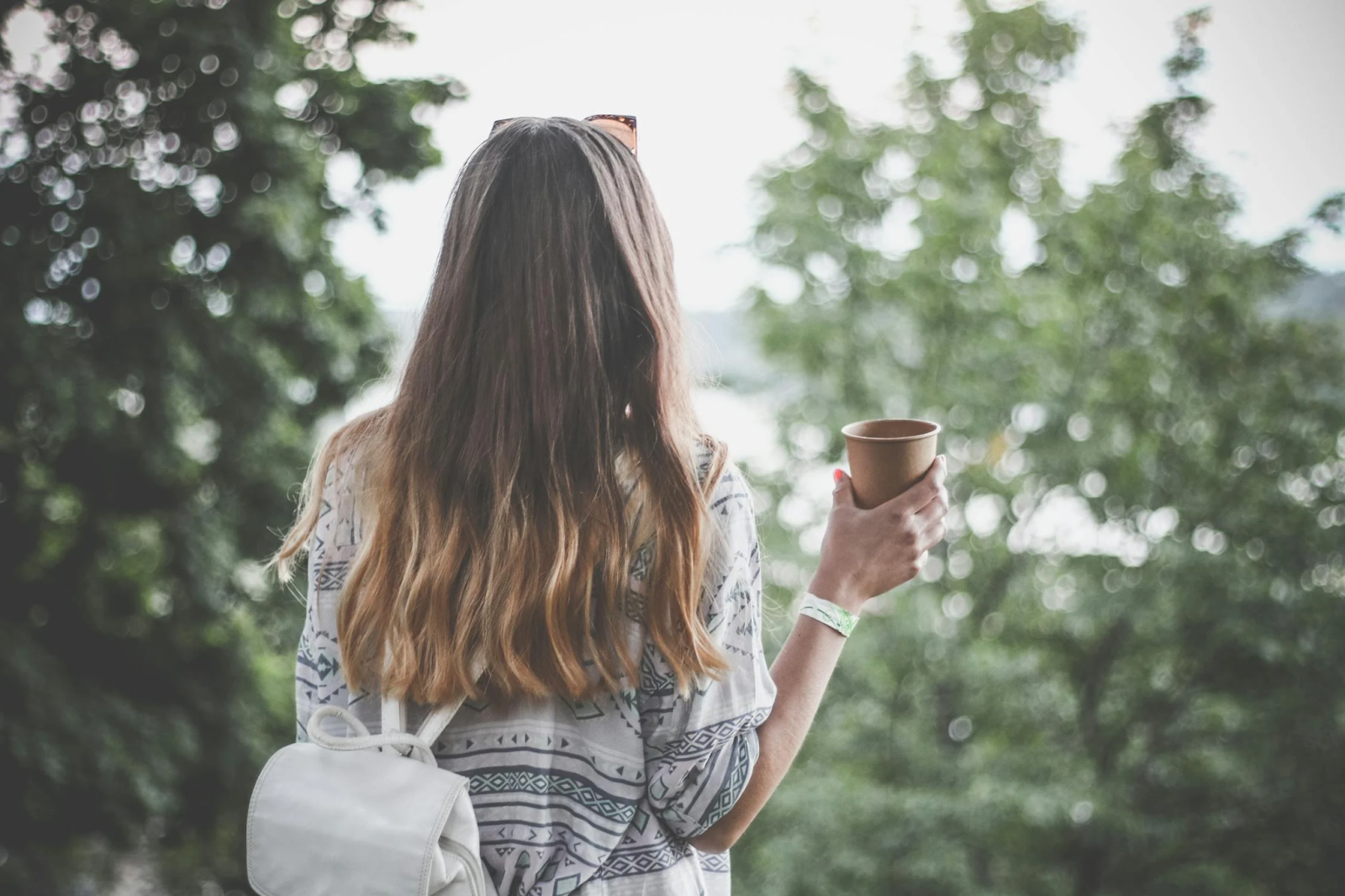 Woman with her back to the screen showing her long hair while holding a cup of coffee. Taken from Pexels