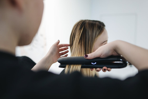 A woman getting her hair styled in a salon with a flat iron.