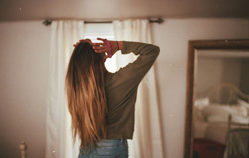 Woman in long-sleeved shirt with long, thick hair, facing away, her fingers on her temples. 