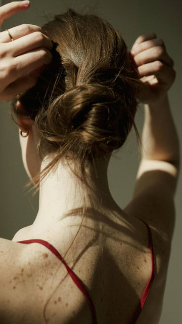 upper back view of a woman with her hands in her short, rolled up hair that's covered with bobby pins, wearing a tank top with red straps.