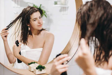Young woman in front of a mirror, spraying product into damp, dark hair.