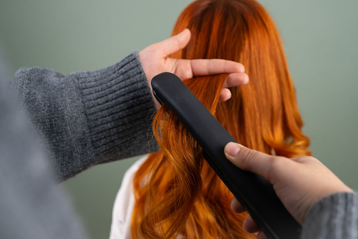 A woman getting her auburn hair styled with a flat iron.