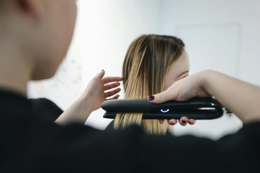 A young woman having her hair styled with a flat iron.