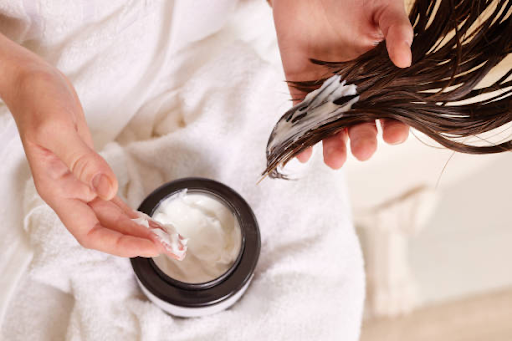 Image of an open hair mask tub being applied to the ends of a person's hair.