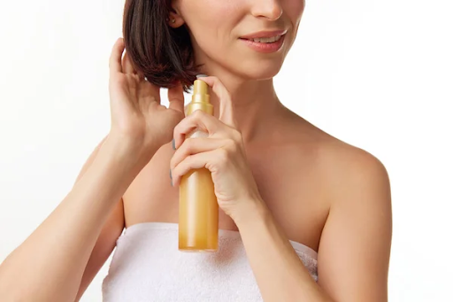 The bottom half view of a woman’s face spraying oil on her hair. Source: deposit photos