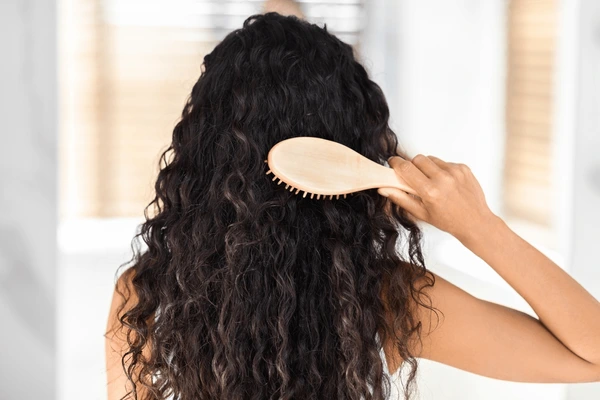 Image of a girl brushing her curly hair with a brush. 