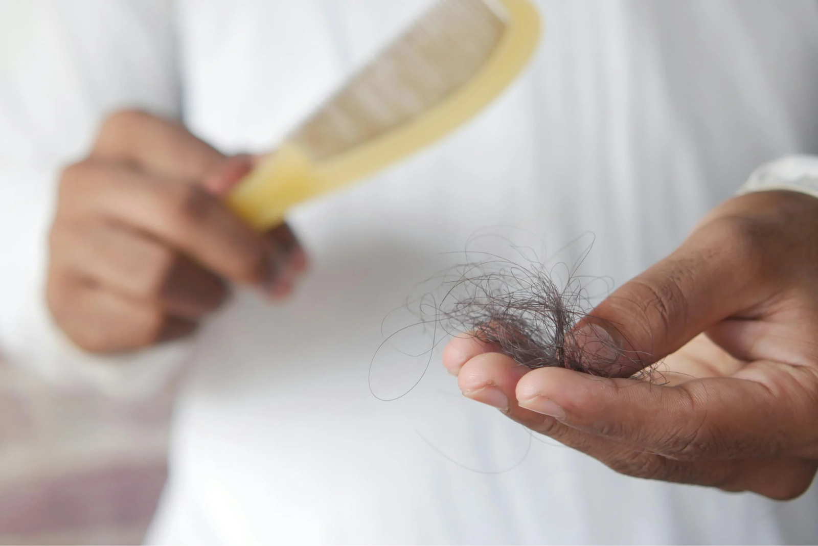 A close-up shot of a person holding some fallen hair next to a hairbrush.