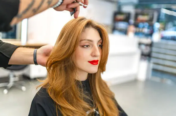 Redhead woman getting a haircut in a long layered style.