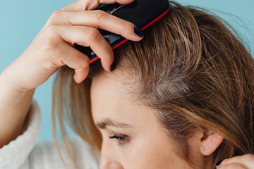 A close-up shot of a woman using a scalp brush on her head.