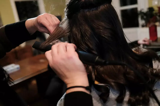A woman styles a woman's hair with a curling iron.