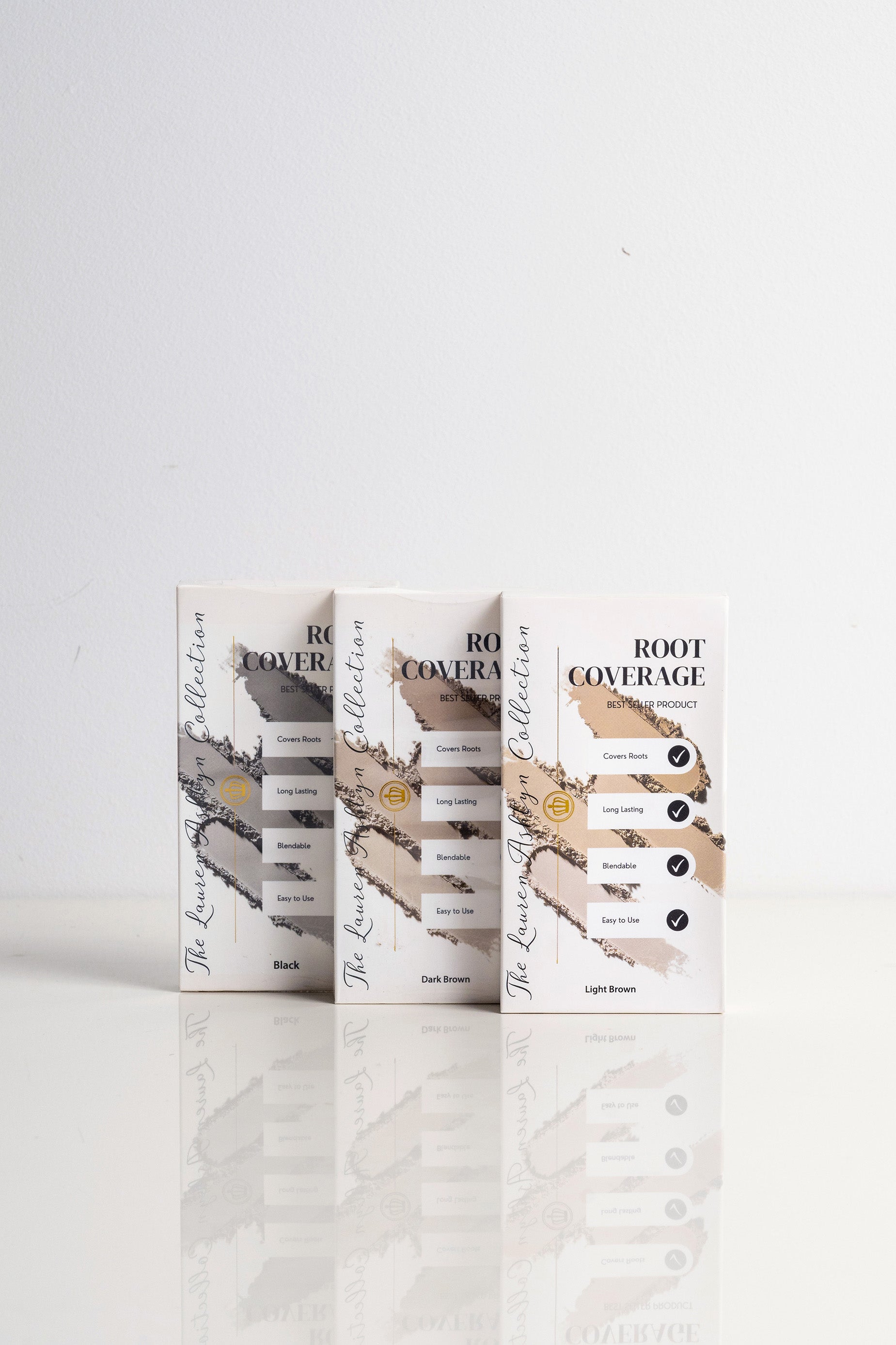 Three boxes of Lauren Ashtyn root coverage powder leaning upright side-by-side in shades of black, dark brown, and light brown.